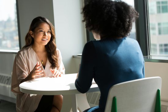 Therapist and client sitting at a round table in a bright office, engaged in supportive conversation during therapy.